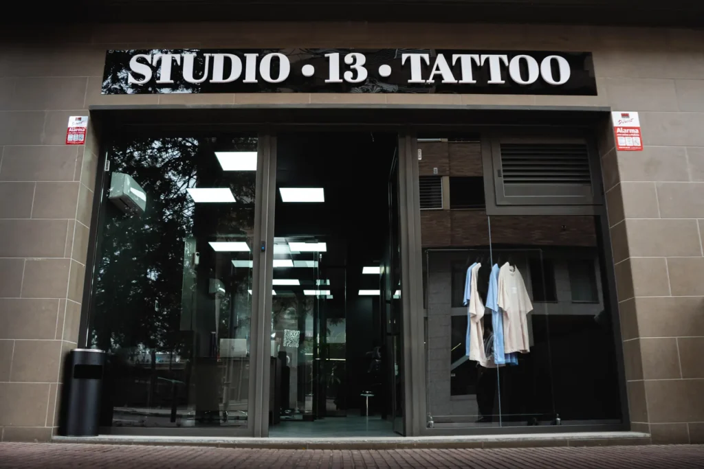Fachada acristalada del local Studio 13 Tattoo tras la reforma, con el rótulo y la retícula de luminarias del interior