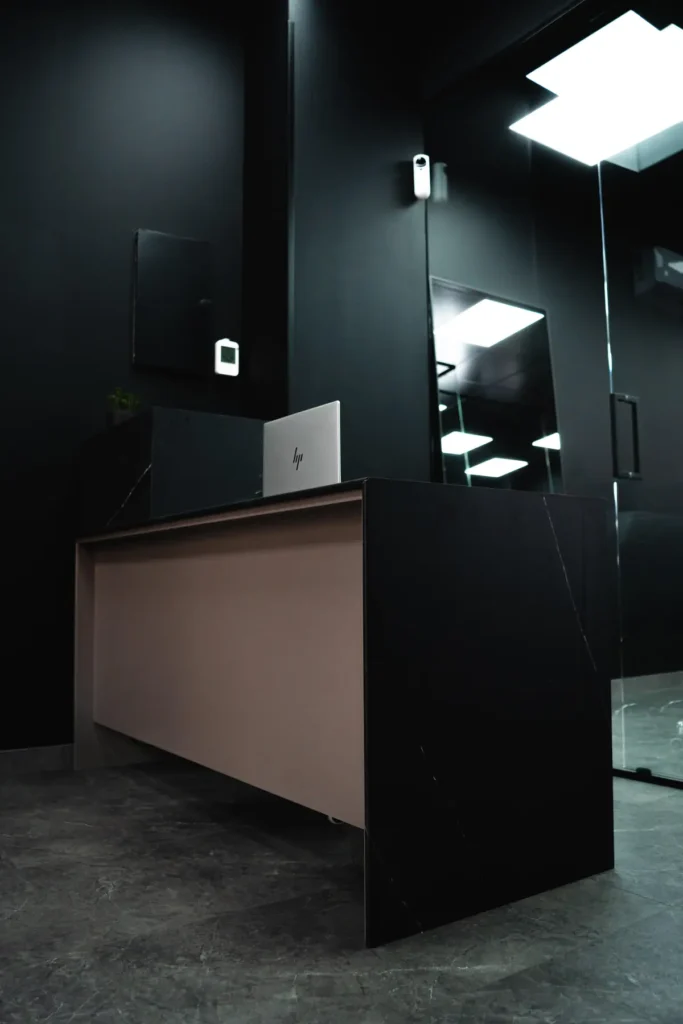Mostrador de recepción en negro y lacado rosa bajo una luminaria de techo